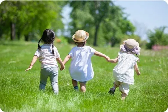 草原で手をつないで走る3人の子どもの後ろ姿