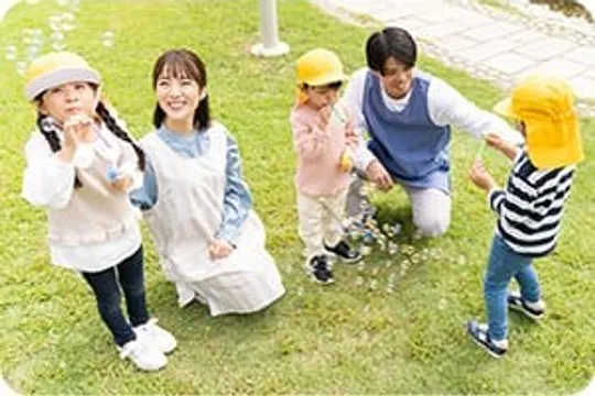 芝生でシャボン玉遊びをする先生と園児