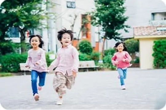 広場を笑顔で走る3人の子どもたち