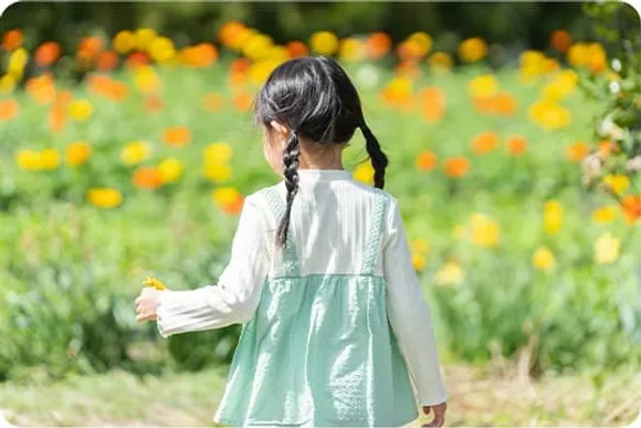 花畑を歩く三つ編みの女の子の後ろ姿