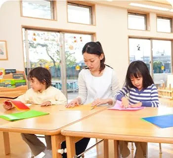 保育室で折り紙をする先生と子どもたち