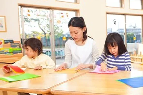 保育室で折り紙をする先生と子どもたち