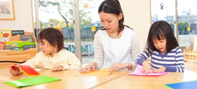 保育室で折り紙を楽しむ先生と子どもたち