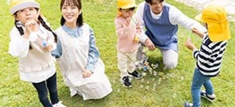 芝生でシャボン玉遊びをする先生と園児