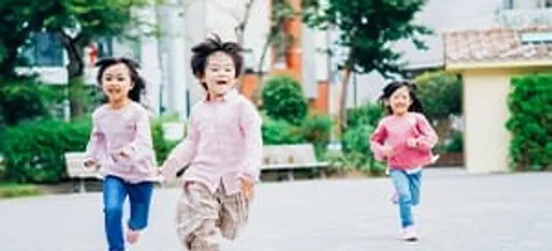 広場を笑顔で走る3人の子どもたち