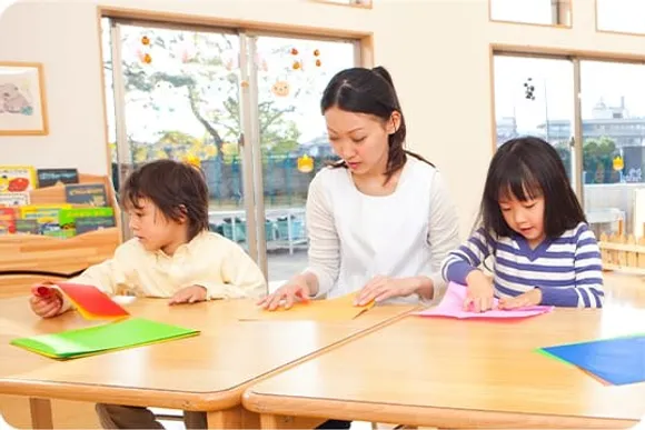 保育室で折り紙を楽しむ先生と子どもたち